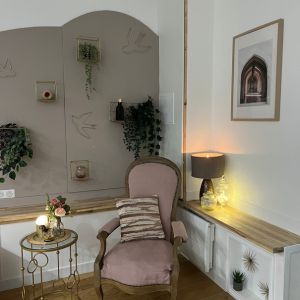 "Un fauteuil vintage restauré avec soin, revêtu d'un rose pâle délicat, trône au centre de la pièce. Sa structure en bois arbore des courbes élégantes, parfaitement assorties à la décoration murale arrondie qui l'entoure. Des touches de blanc doré ajoutent une touche de sophistication, tandis que des plantes égayent l'espace avec leur verdure apaisante. Une harmonie subtile de couleurs rose, blanc doré et bois crée une atmosphère chaleureuse et accueillante.1. Fauteuil 2. Vintage 3. Restauré 4. Rose pâle 5. Bois 6. Décoration murale 7. Courbes élégantes 8. Blanc doré 9. Plantes 10. Atmosphère harmonieuse